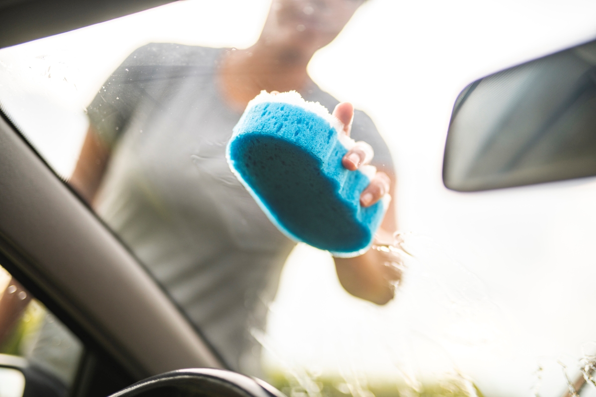 Person rubbing car window with sponge.