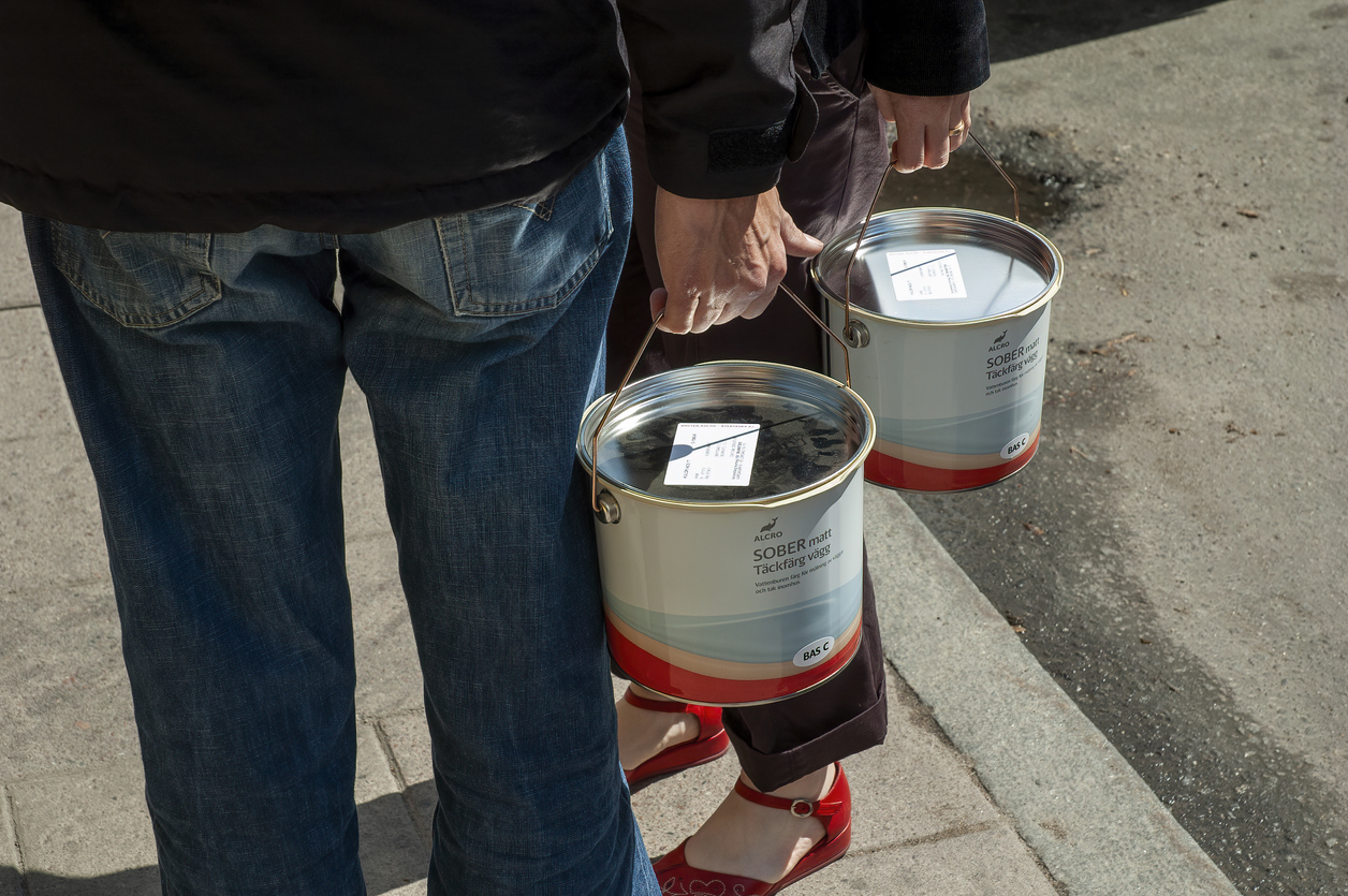 two people carry a paint can each with paint