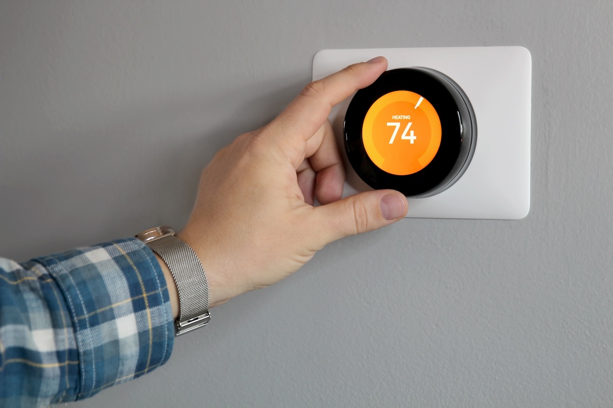 A person turning up the home thermostat to 74 degrees which can spike gas bills during cold times of year.