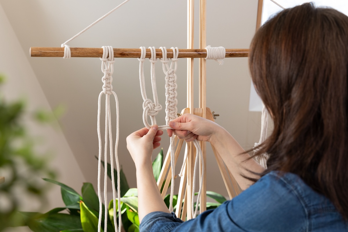 A person using macrame to create a fiber wall hanging for the home.