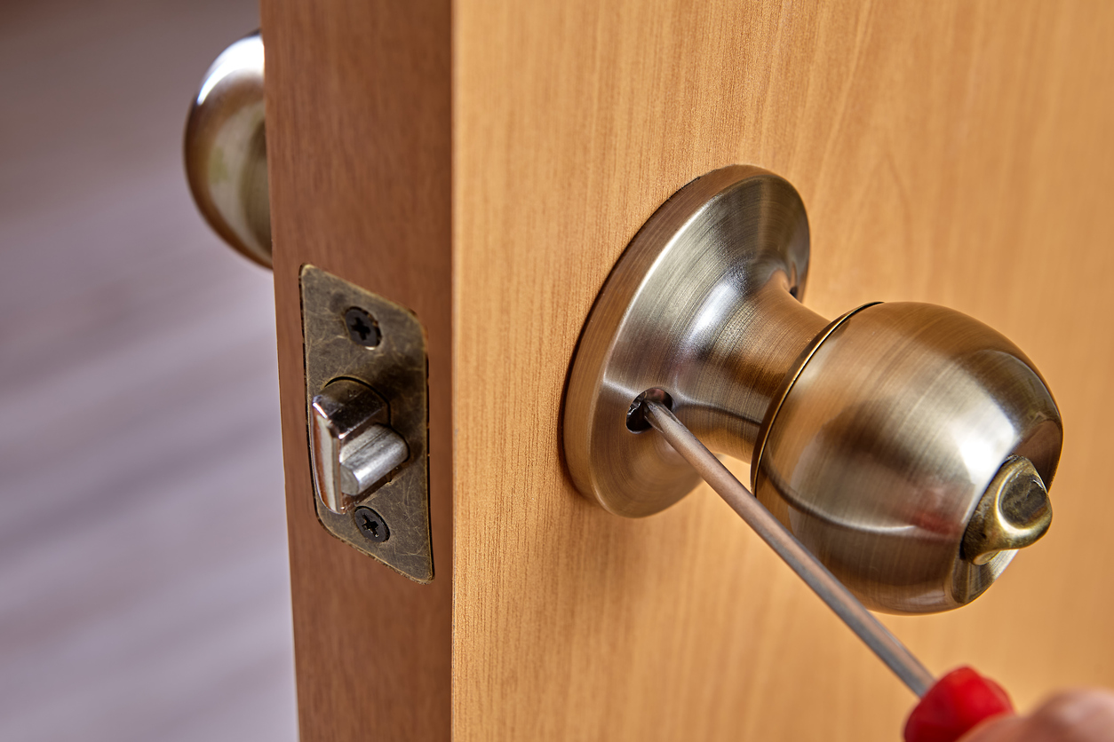 Locksmith fixes door handle rose with screw, using screwdriver.