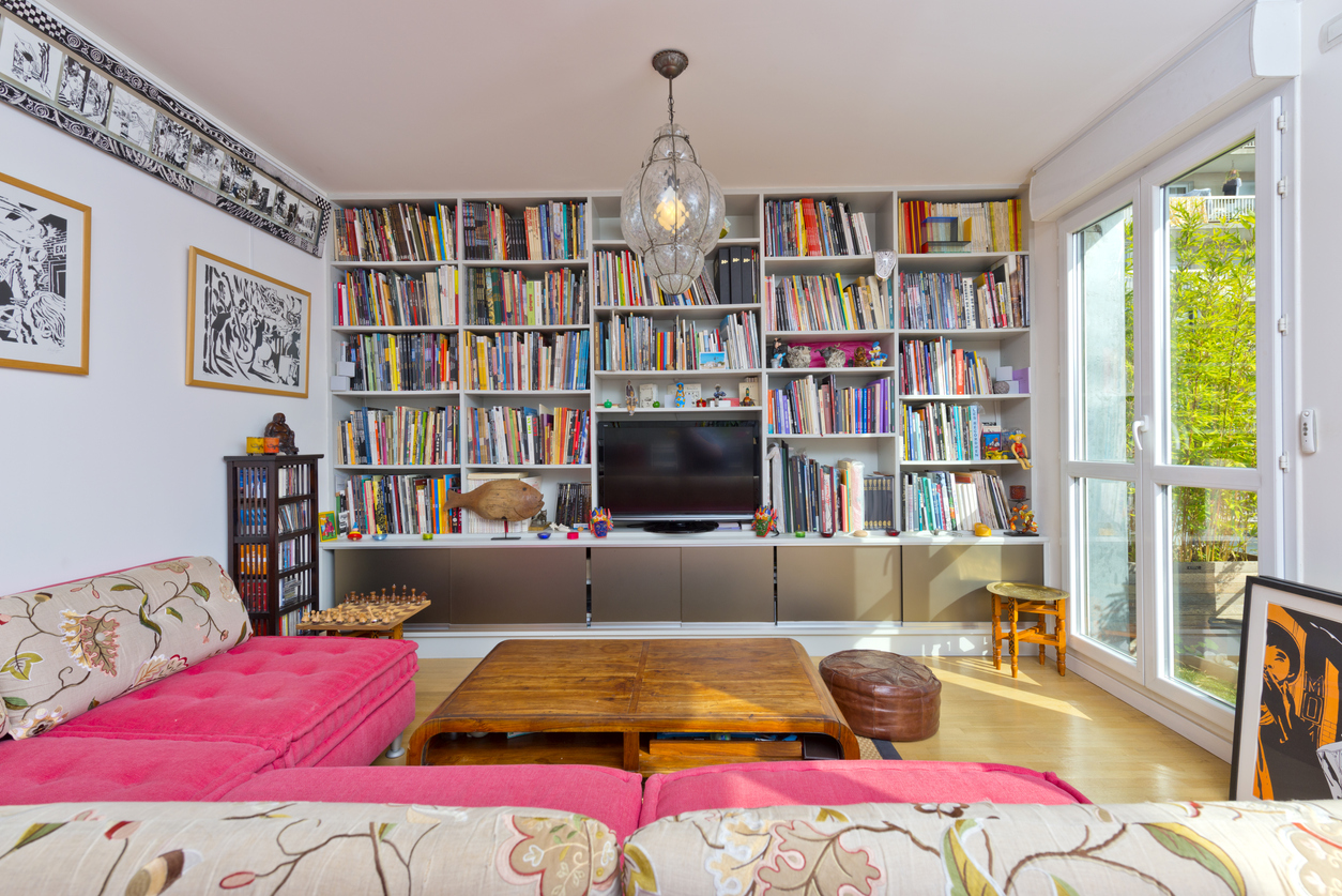 A-wall-of-built-in-bookcases-is-full-of-colorful-books-in-a-living-room-with-bright-colors-and-art.