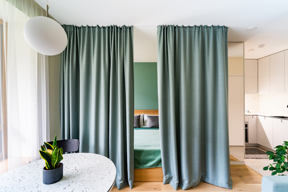 Sage-green-curtains-divide-a-room-to-give-privacy-to-a-wood-and-green-bed.