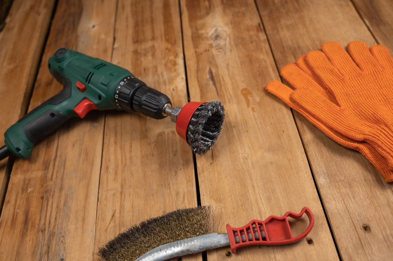 Electric drill, knot cup wire brush, metal brush and orange gloves. Hand and power tools lie on the boards. Woodworking. Top view. Selective focus.