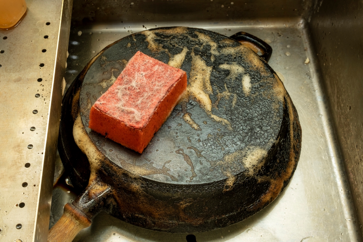 Cleaning dirty cast iron pan with sponge.