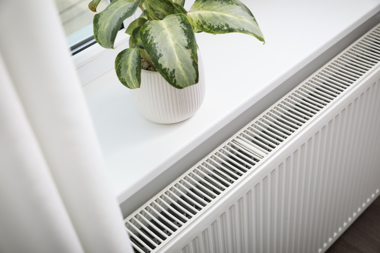 Beautiful houseplant on window sill and modern radiator at home. Central heating system