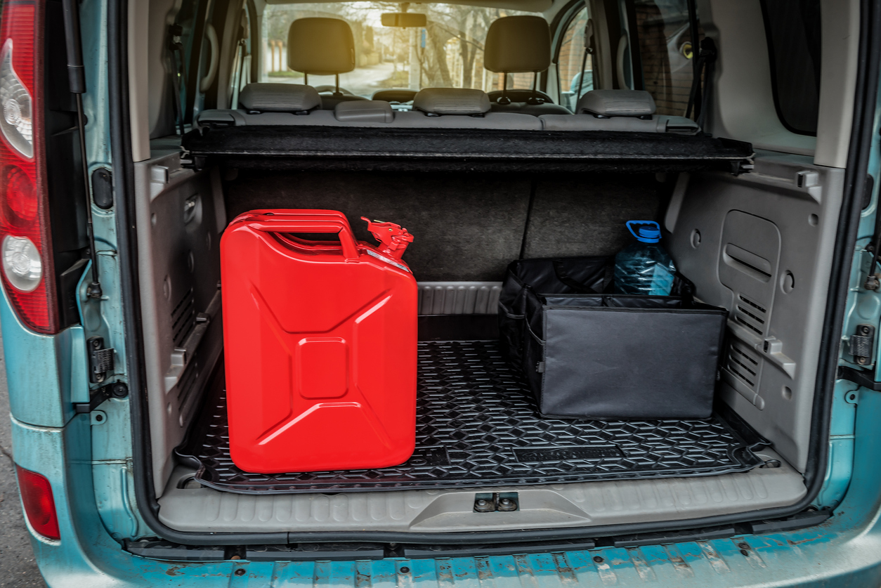 Red metal canister tank with gasoline or diesel in the trunk of the car. Transportation theme