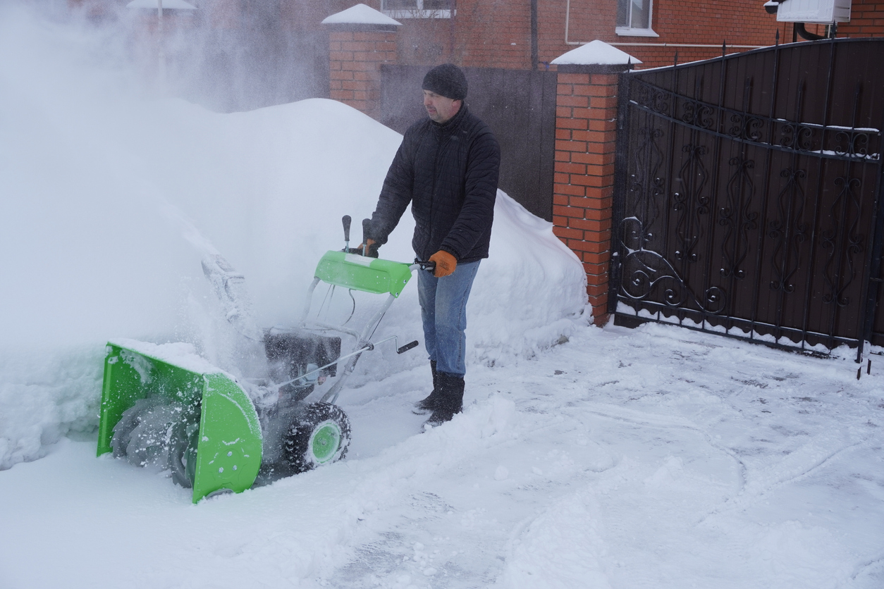 A man cleans snow in the winter in the courtyard of the house, man cleaning snow with a snow blower