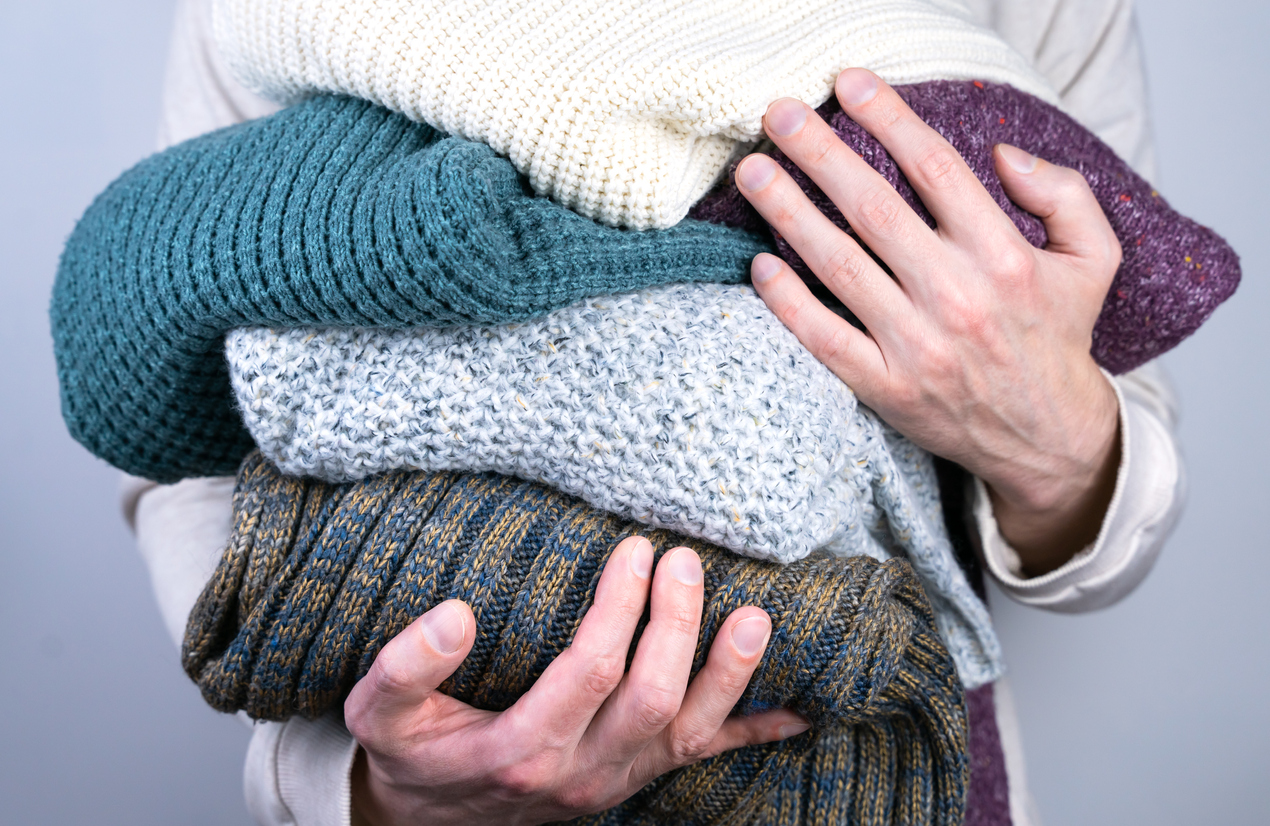 Men's hands hold warm knitted sweaters. Warm winter clothes. Seasonal clothes. Selective focus.