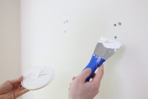 Patching small holes in wall with spatula.