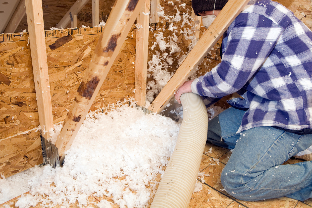 Worker Spraying Insulation between Attic Floor Joists and Roof Trusses
