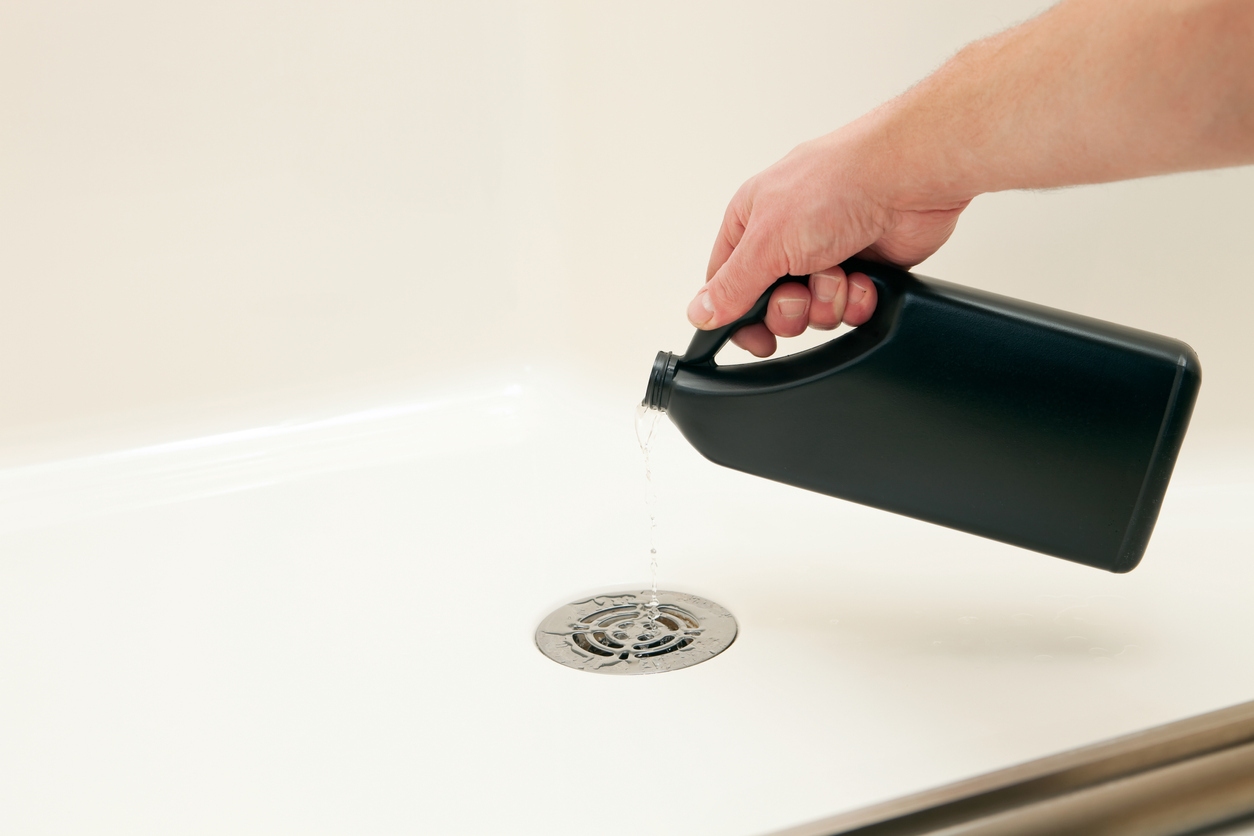 A male hand is pouring liquid drain cleaner into a shower drain to dissolve a clog and improve water flow.