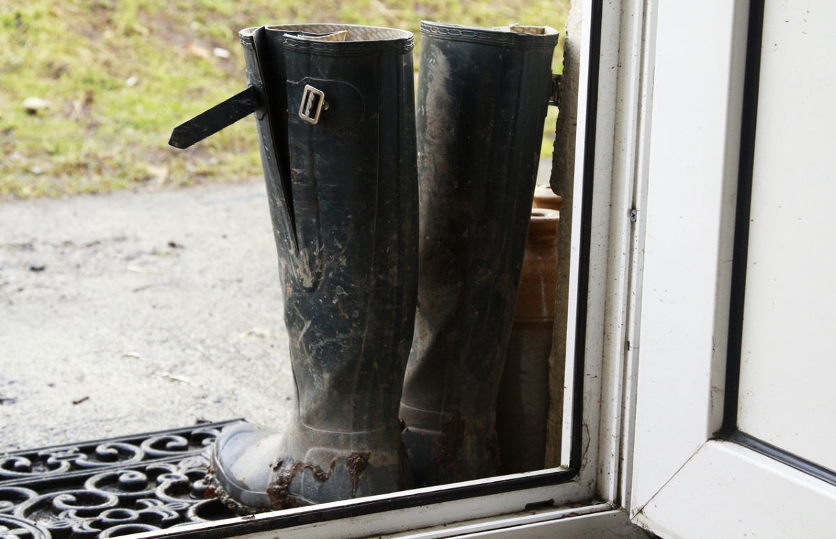 Pair of black muddy boots by front door.