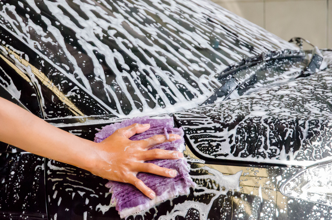 A hand washing a car with a microfiber cloth