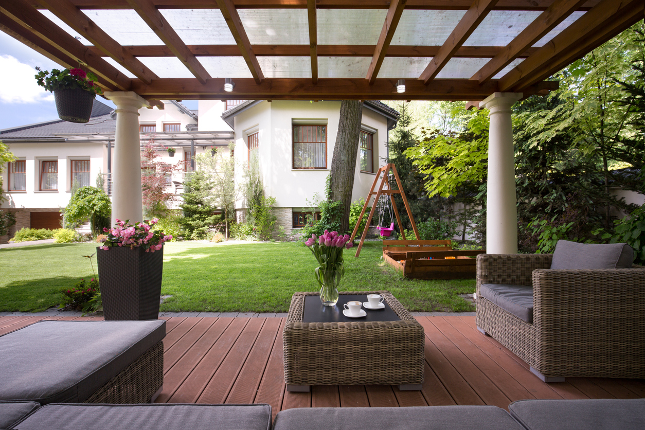 Stylish home with backdoor pergola with glass panes and patio furniture.