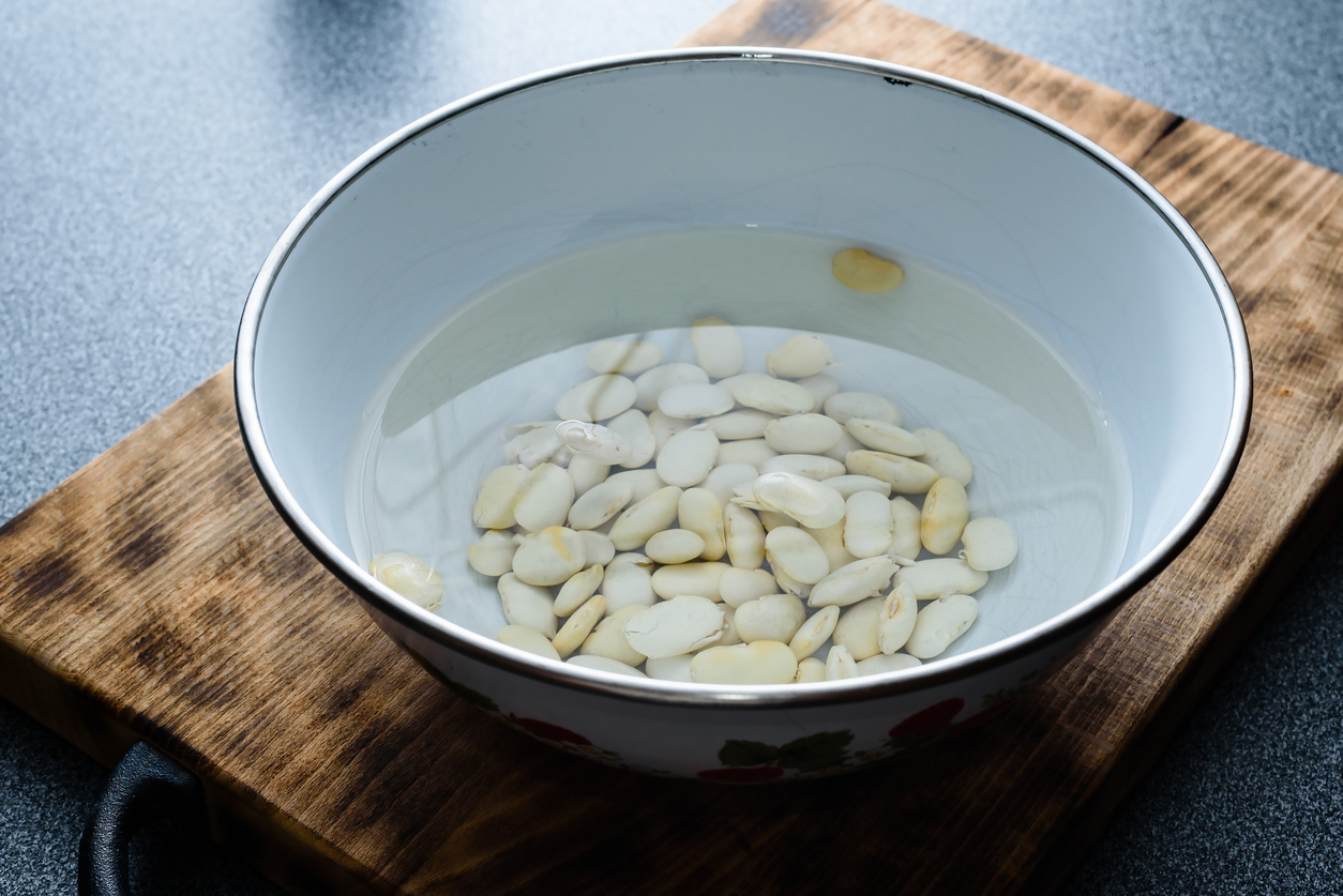 Large white beans soaking in water on a dark wooden cutting board.
