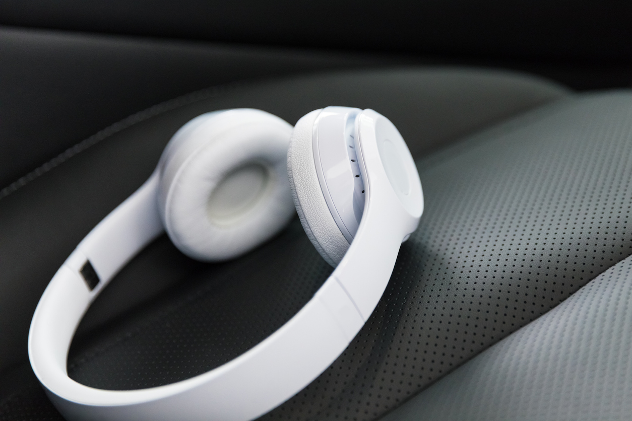 Modern wireless internet technology concept: macro view of the white wireless headphones on the black leather car seat with selective focus effect