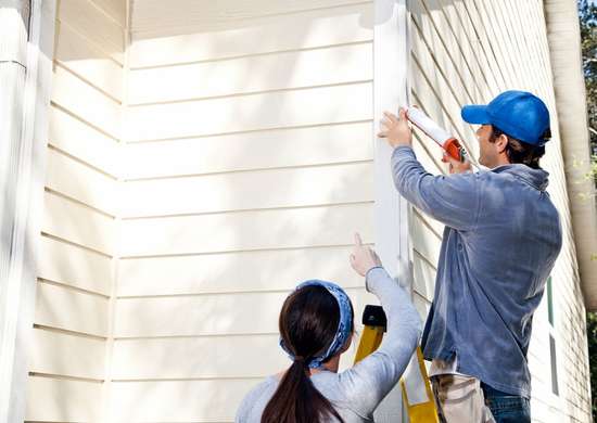Two people caulking house for pest control