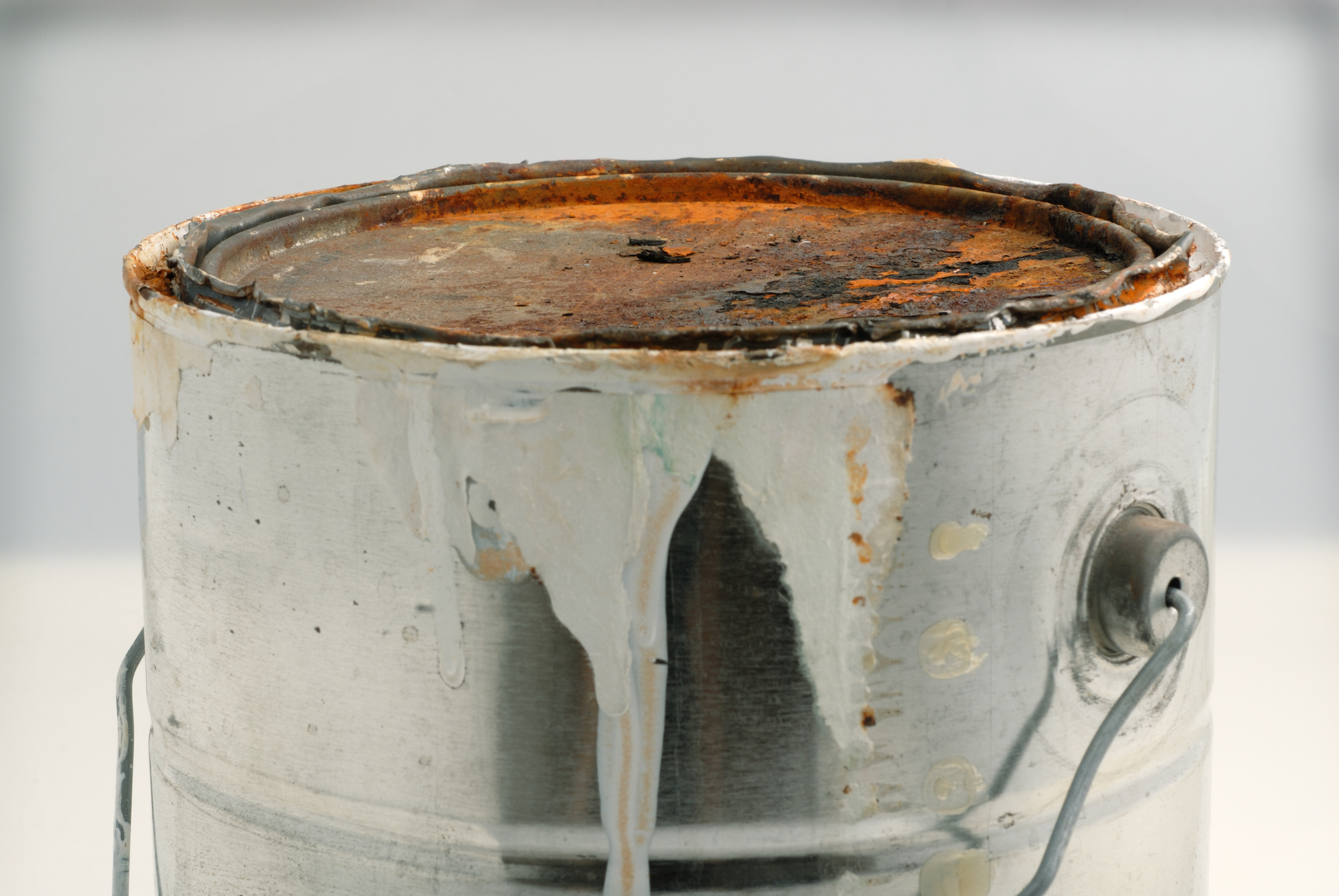 Gallon paint can with rusted lid and white paint dripping over the sides.