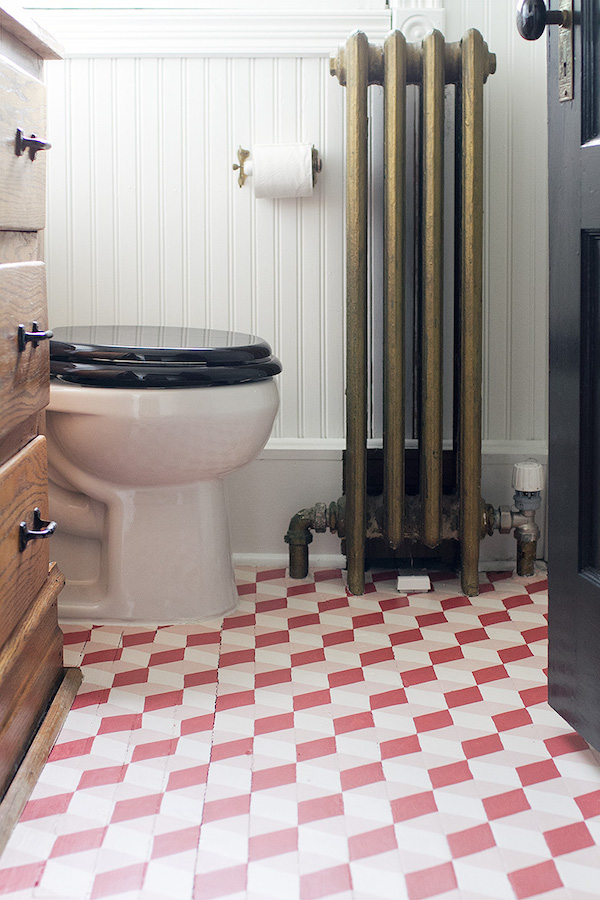 Vintage bathroom with radiator and painted tile floors in a pink tumbling dice pattern.