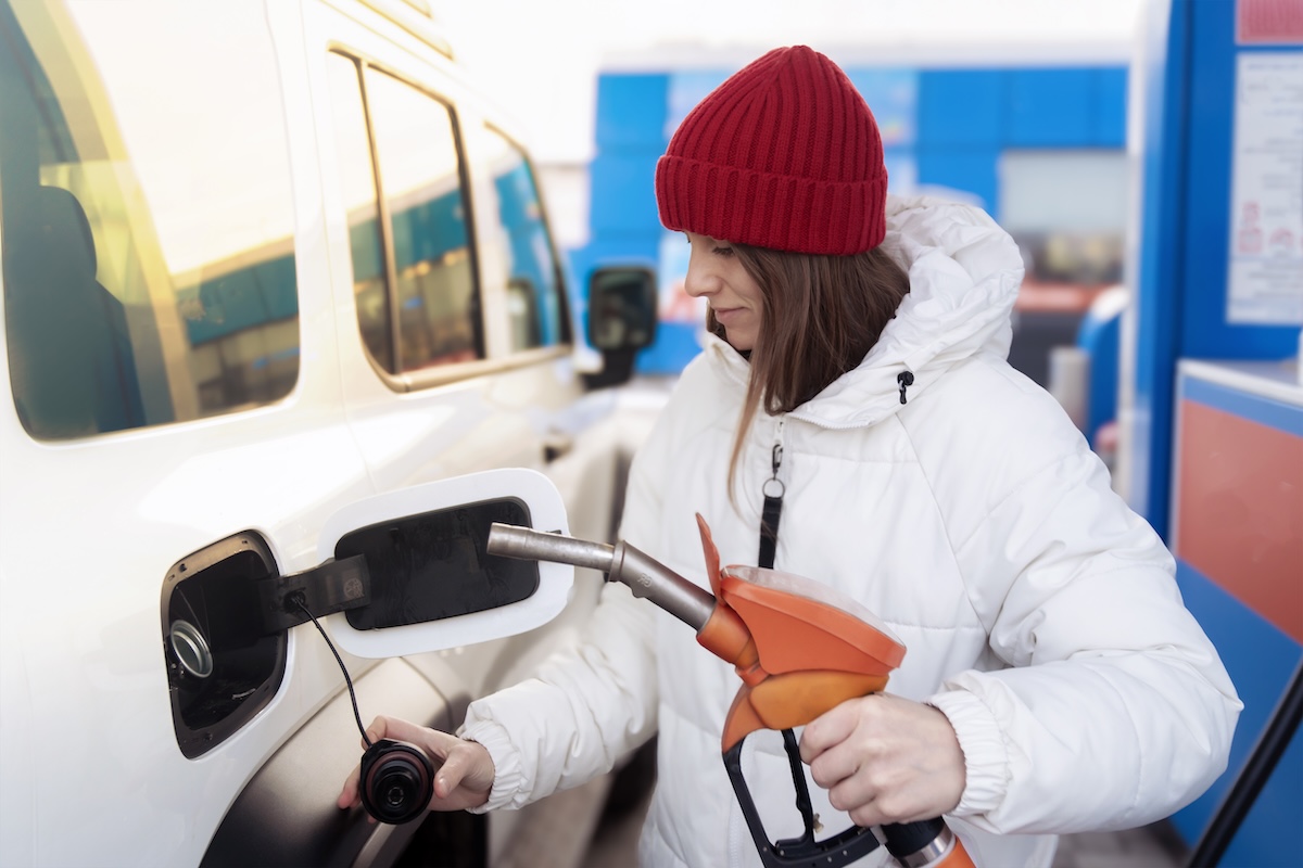 A woman in a white down jacket refueling her car at a gas station.