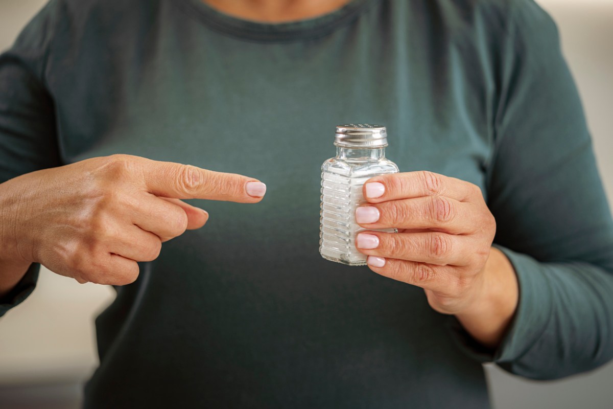 Woman holding salt shaker in left hand and pointing to it with her right index finger.