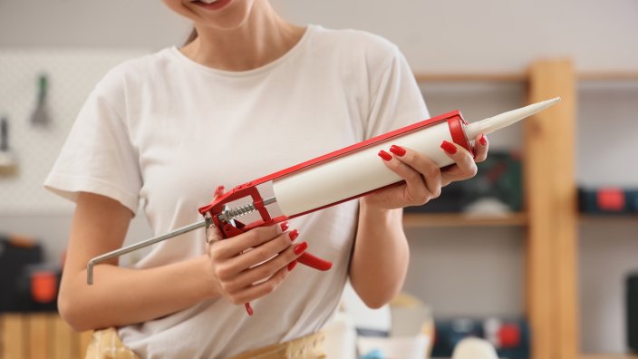 Young woman with sealant during repair in room, closeup.