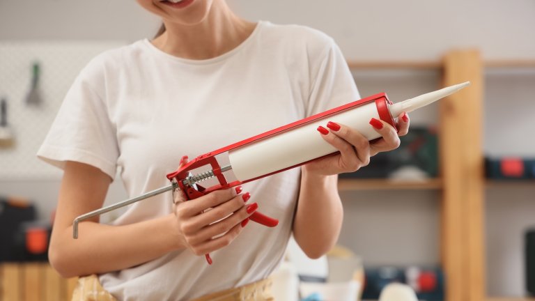 Young woman with sealant during repair in room, closeup.