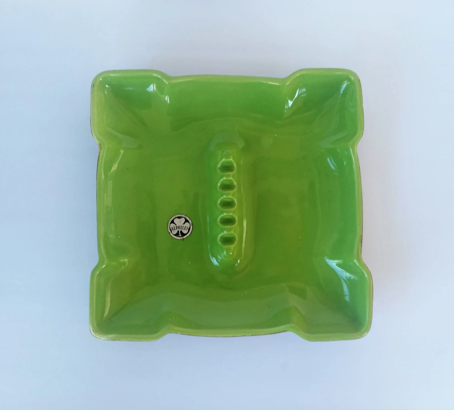 A-vintage-green-ceramic-ashtray-with-original-brand-lable-sits-on-a-white-background.