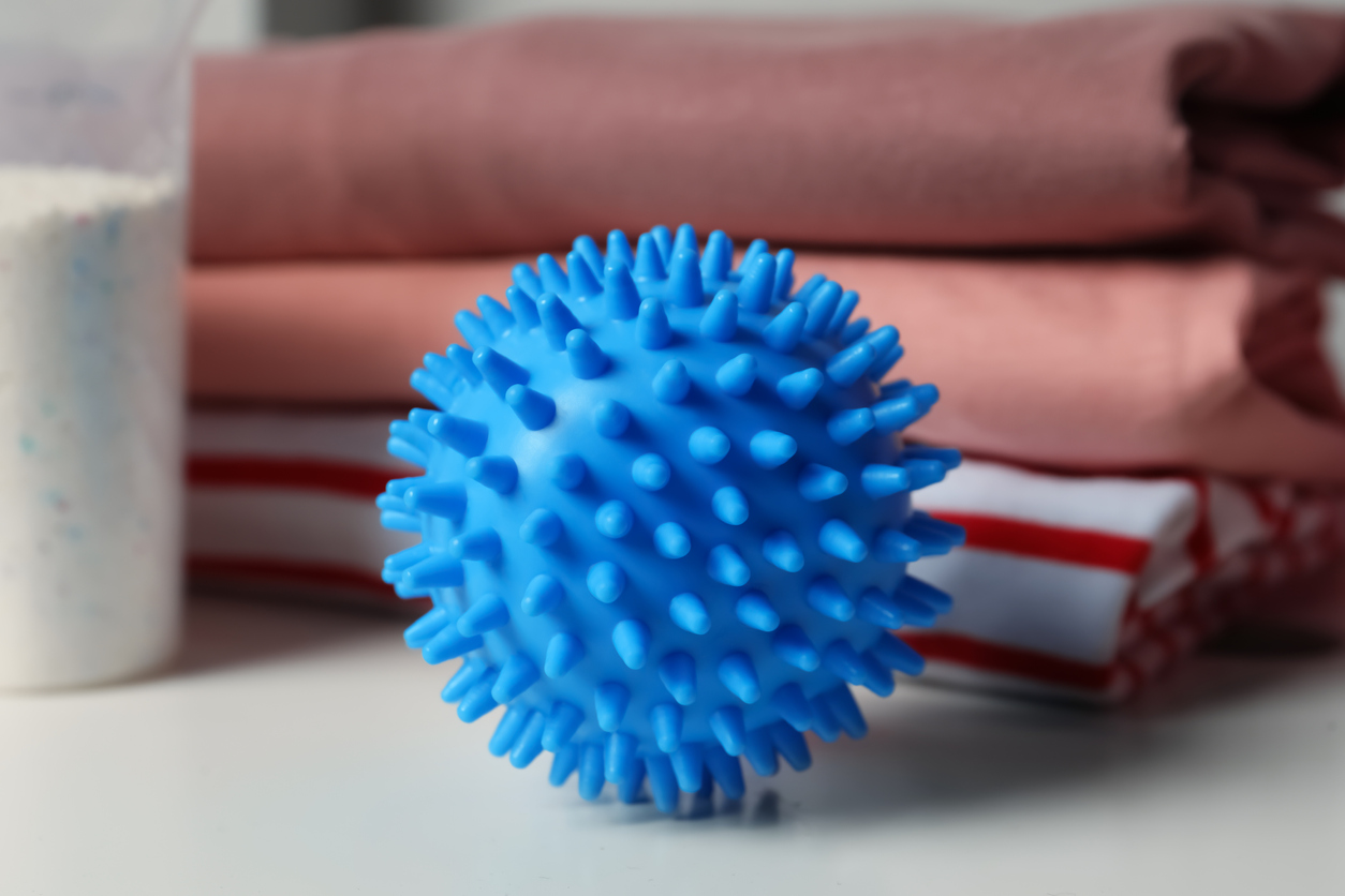 A blue plastic dryer ball sitting atop a dryer in front of a cup of powdered laundry detergent and folded clothes.