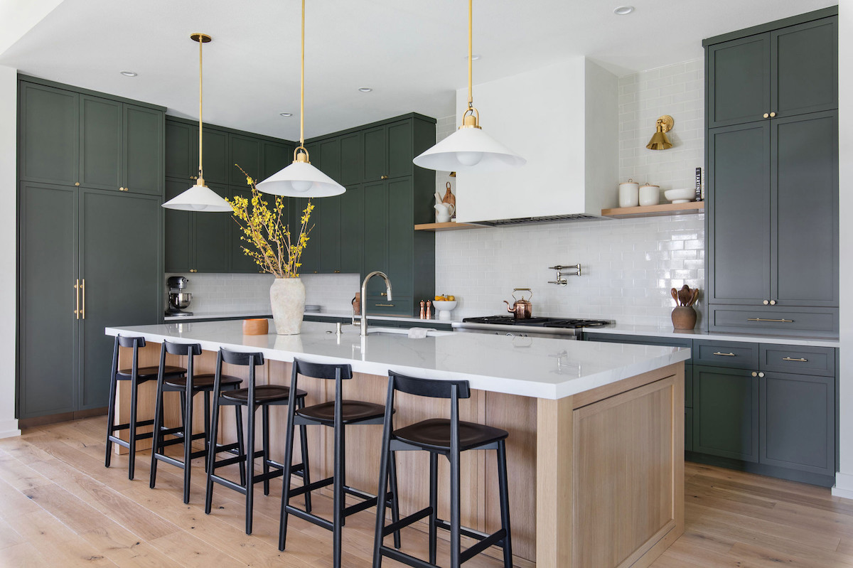 A modern kitchen has cabinets in a dark gray with green tint and a pale wood island.