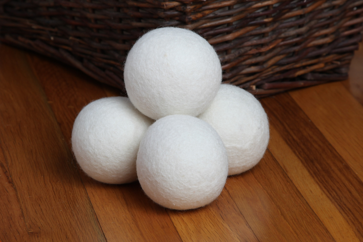 A stack of five wool dryer balls sitting next to a wicker basket on hardwood flooring.