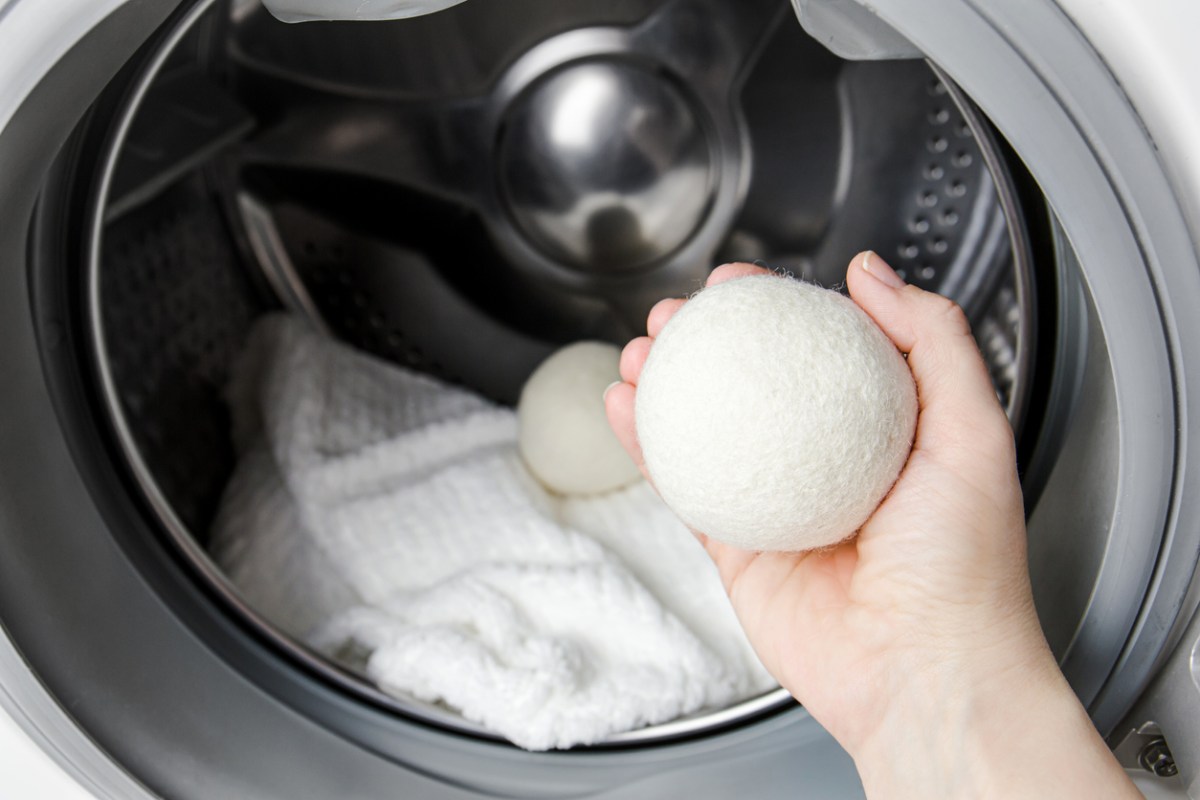 A person holding a wool dryer ball in front of an open front-loading dryer while doing laundry.