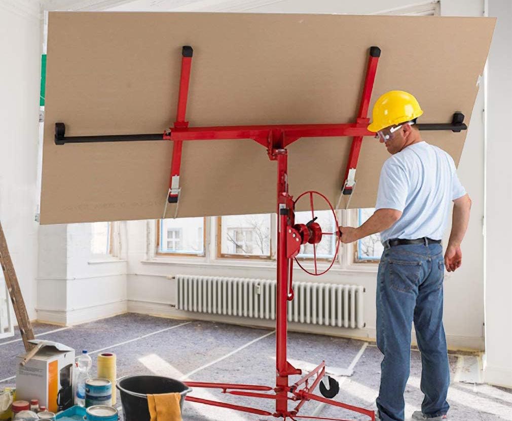 A person using the FDW Drywall Panel Hoist to hold a large drywall panel in a room undergoing a remodel.