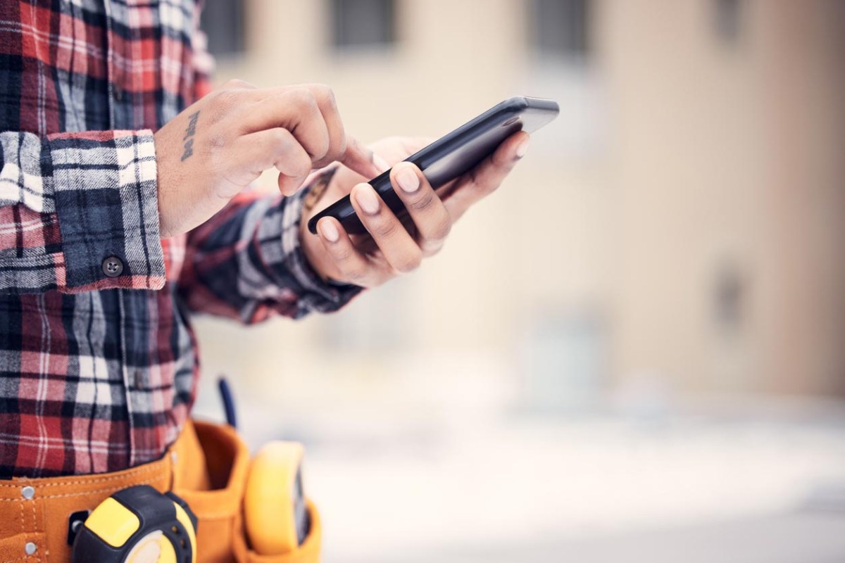 A handyman in flannel and a tool belt is on a smart phone.