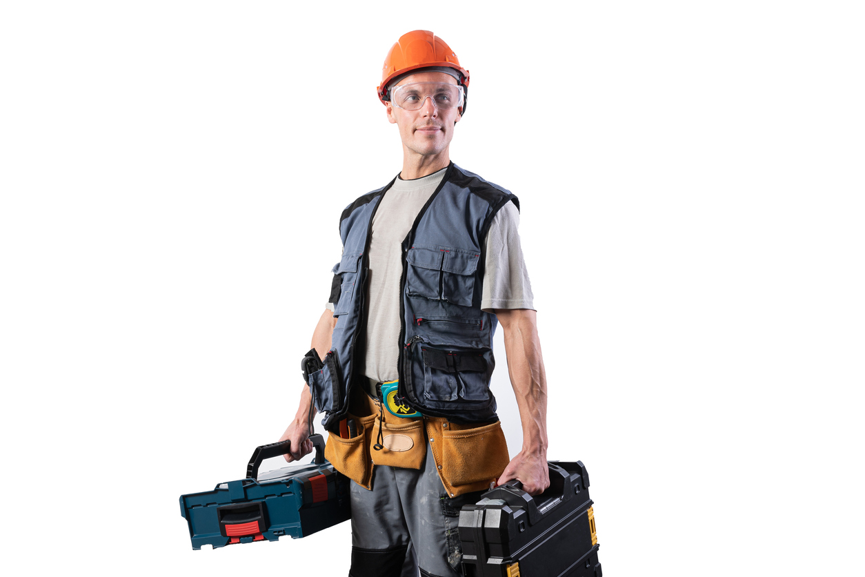 A person wearing a tool vest, tool belt, and hard hat while carrying a power tool case and tool box.