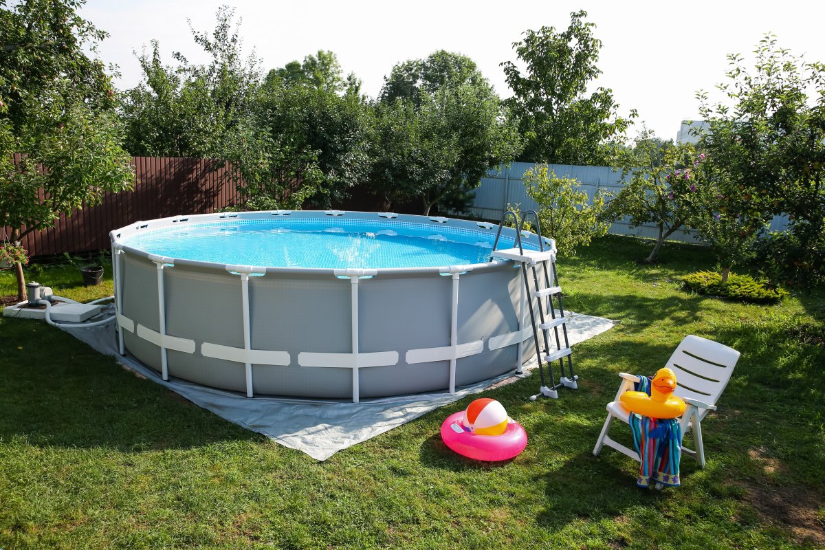 An above-ground swimming pool in a backyard with toys and a lawn chair.