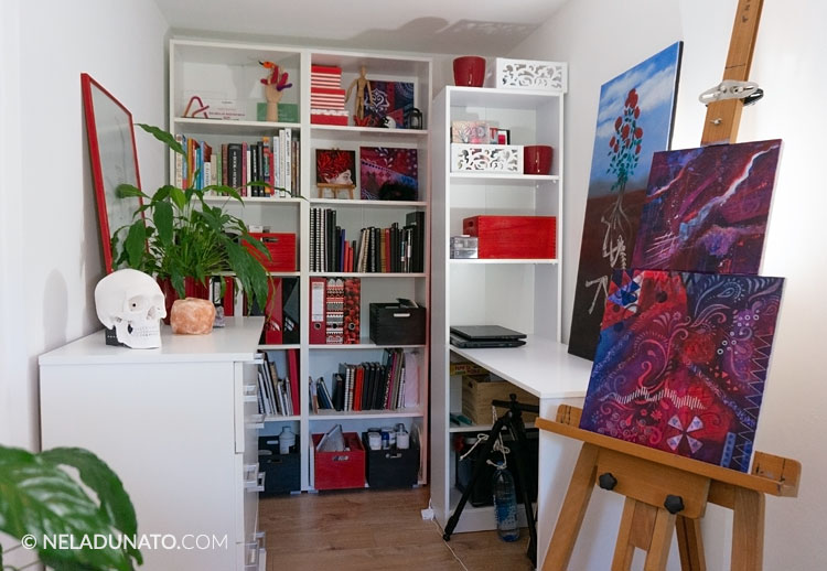 Art studio with red and white decor sitting on a large bookcase behind an easel.