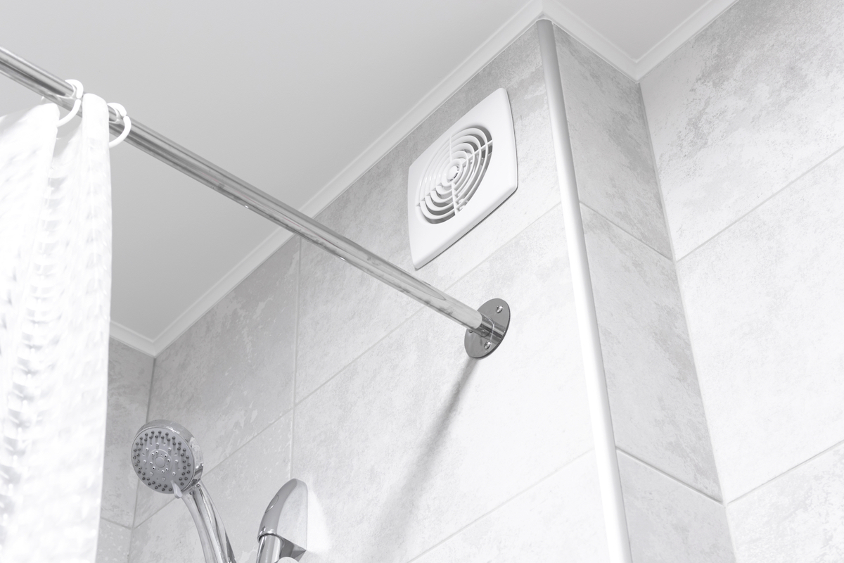 Bathroom exhaust fan near shower rod in a modern grey bathroom.