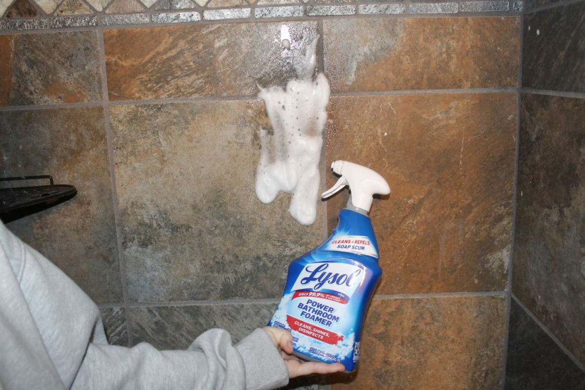 A person holding a spray bottle of Lysol Power Bathroom Foamer Cleaner after spraying it on shower tile during testing.