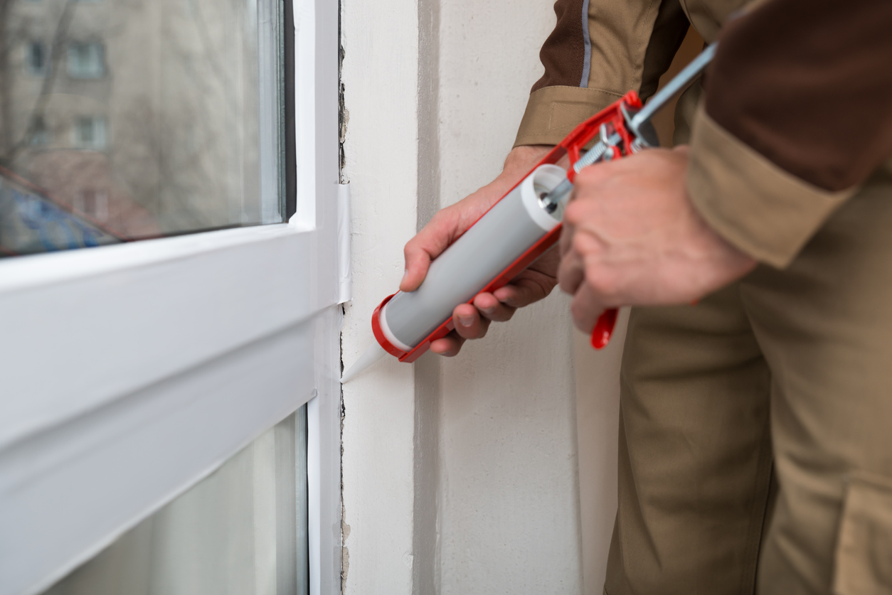 Homeowner applying silicone sealant with caulking gun to weatherproof door.