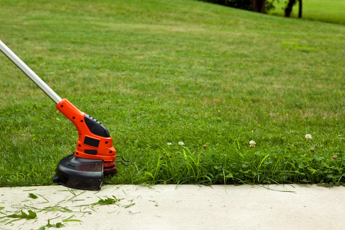 A person uses a string trimmer to edge the lawn along the driveway.