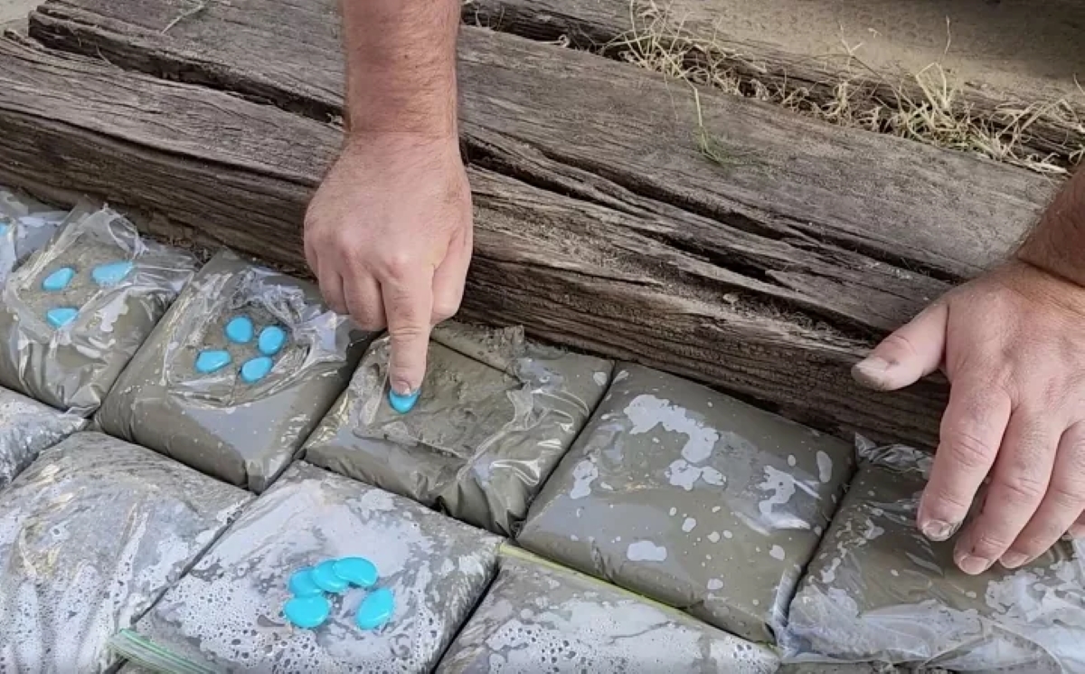 Person placing blue stones on exposed wet concrete in plastic bags.