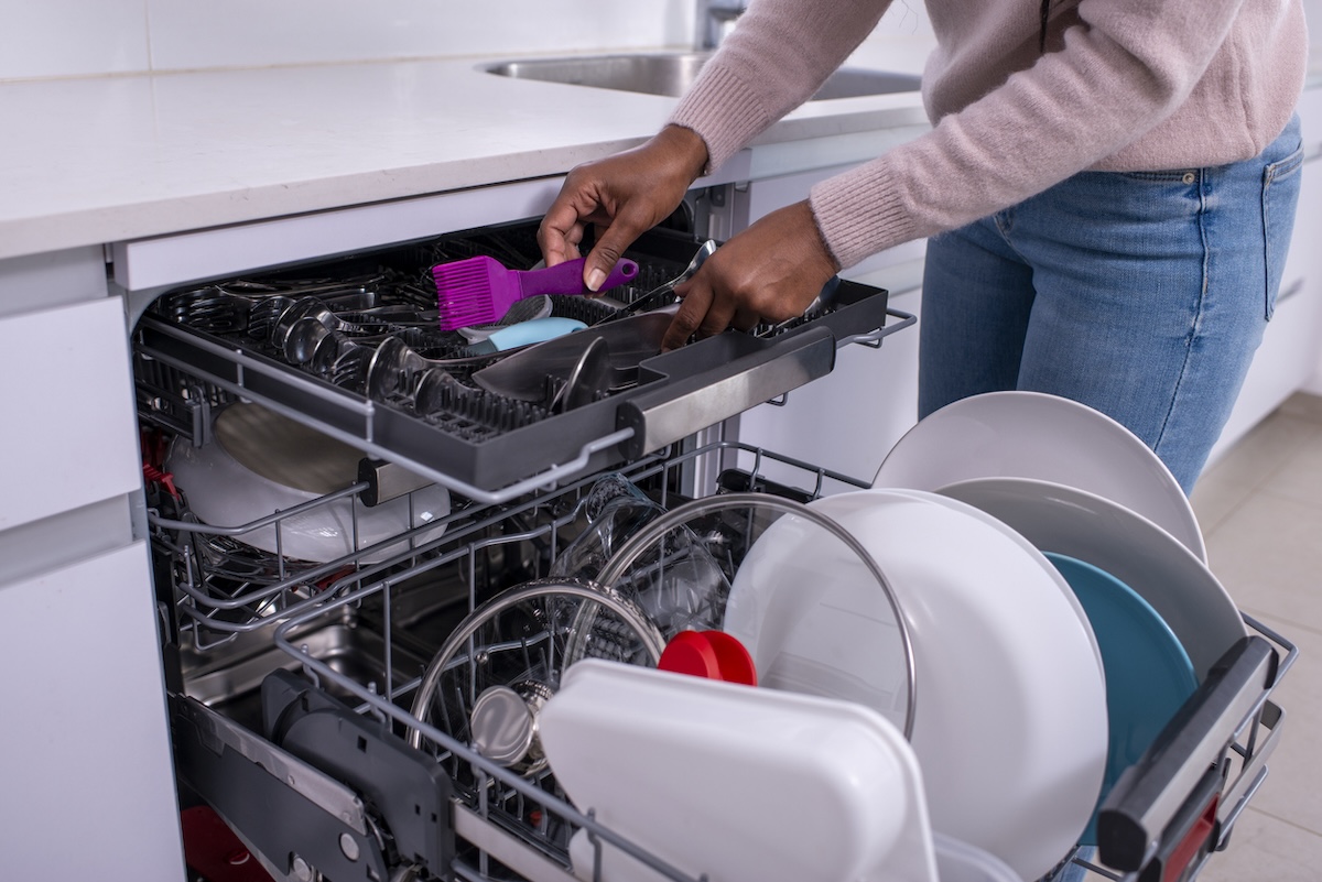 A person loading a dishwasher in their kitchen.