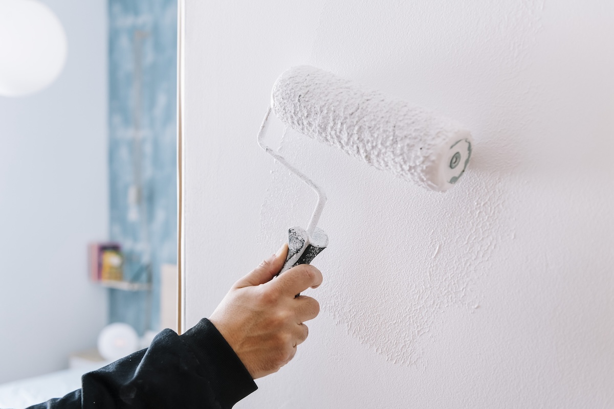 A person using a roller to touch up paint on walls.