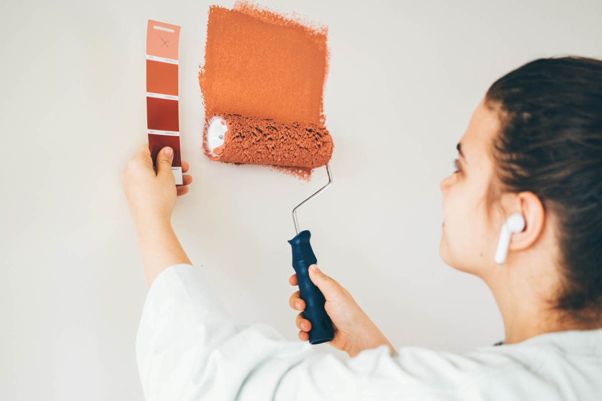 Woman holding paint sample while painting wall.