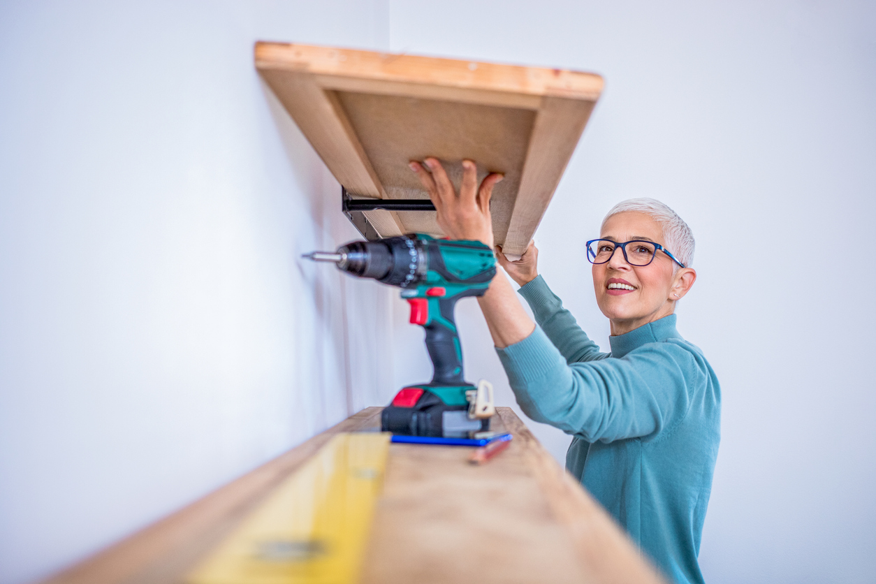 A-person-holds-a-wood-shelf-while-putting-it-up-using-a-drill.