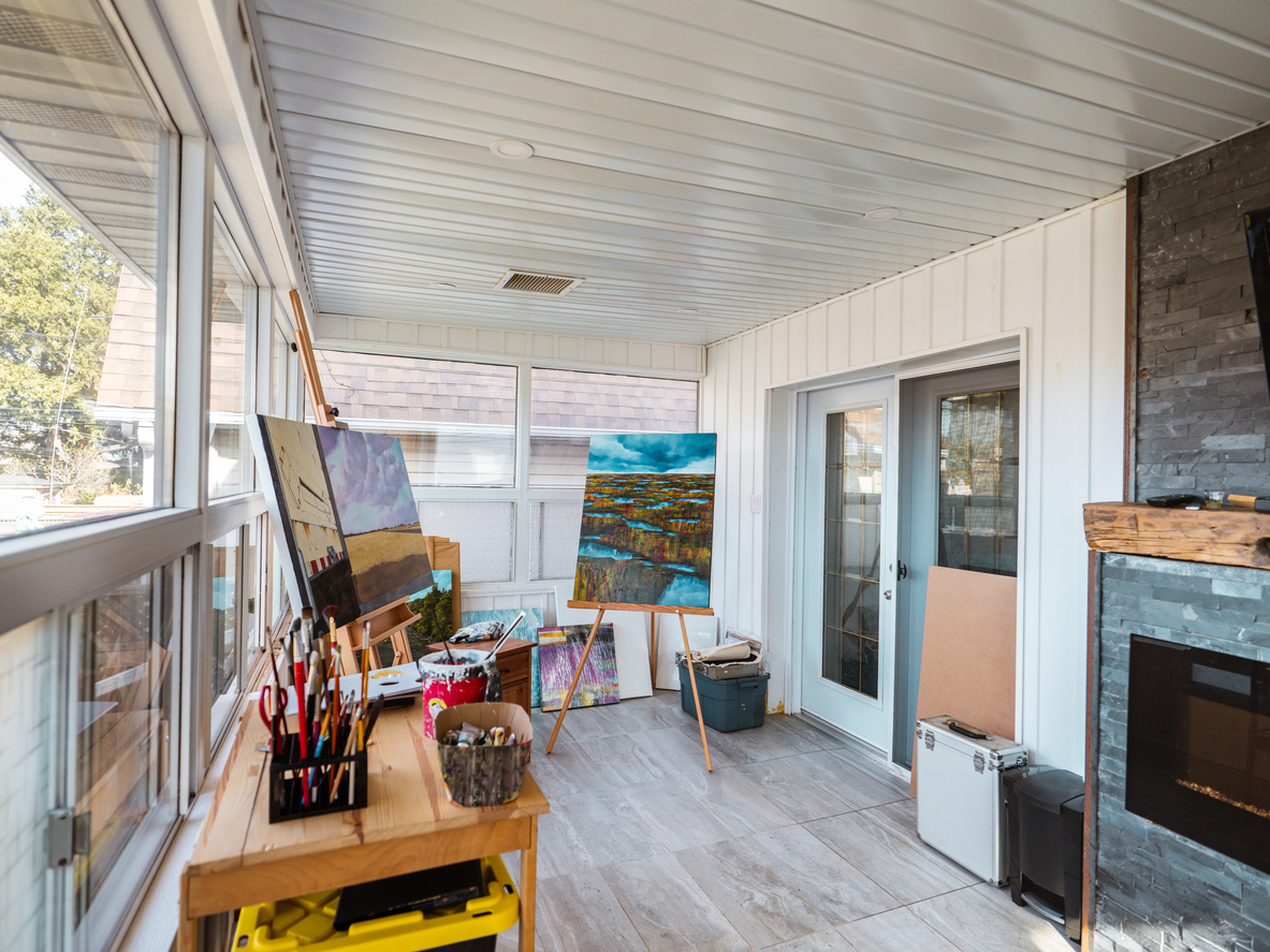 Home art studio on house porch with easels, canvases, and organized materials.