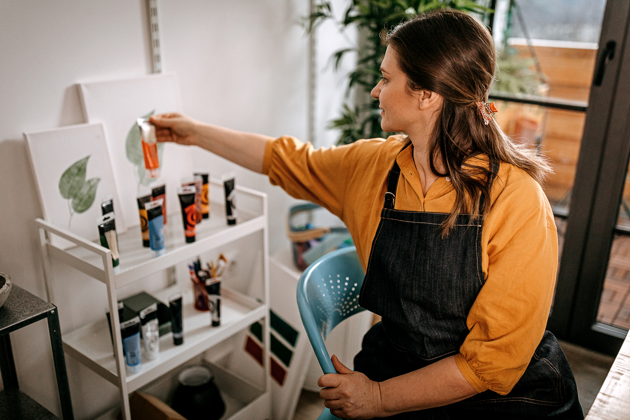 Woman in yellow blouse and black apron organizes paints on a tiered cart.