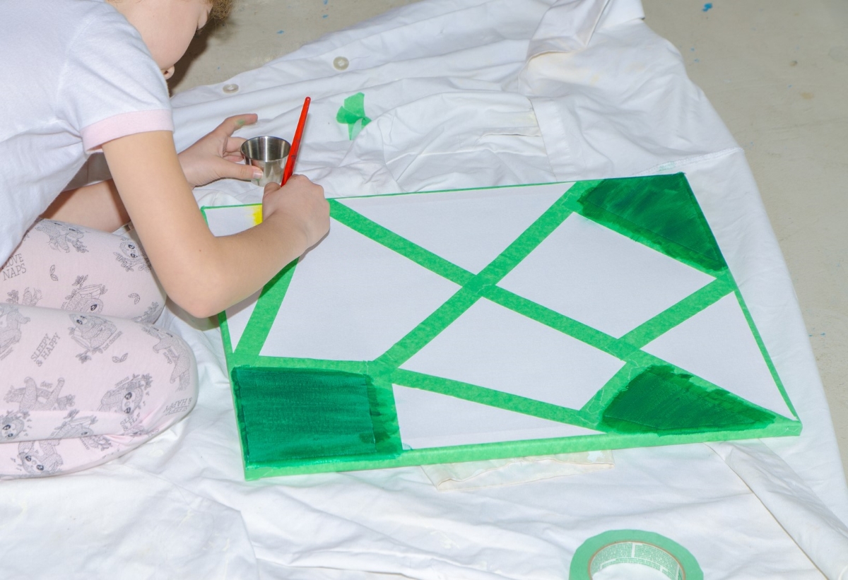 Child painting canvas outlined with tape.